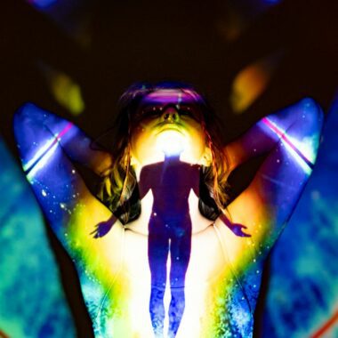 A silhouette emerges through colorful projections, evoking spirituality and energy.